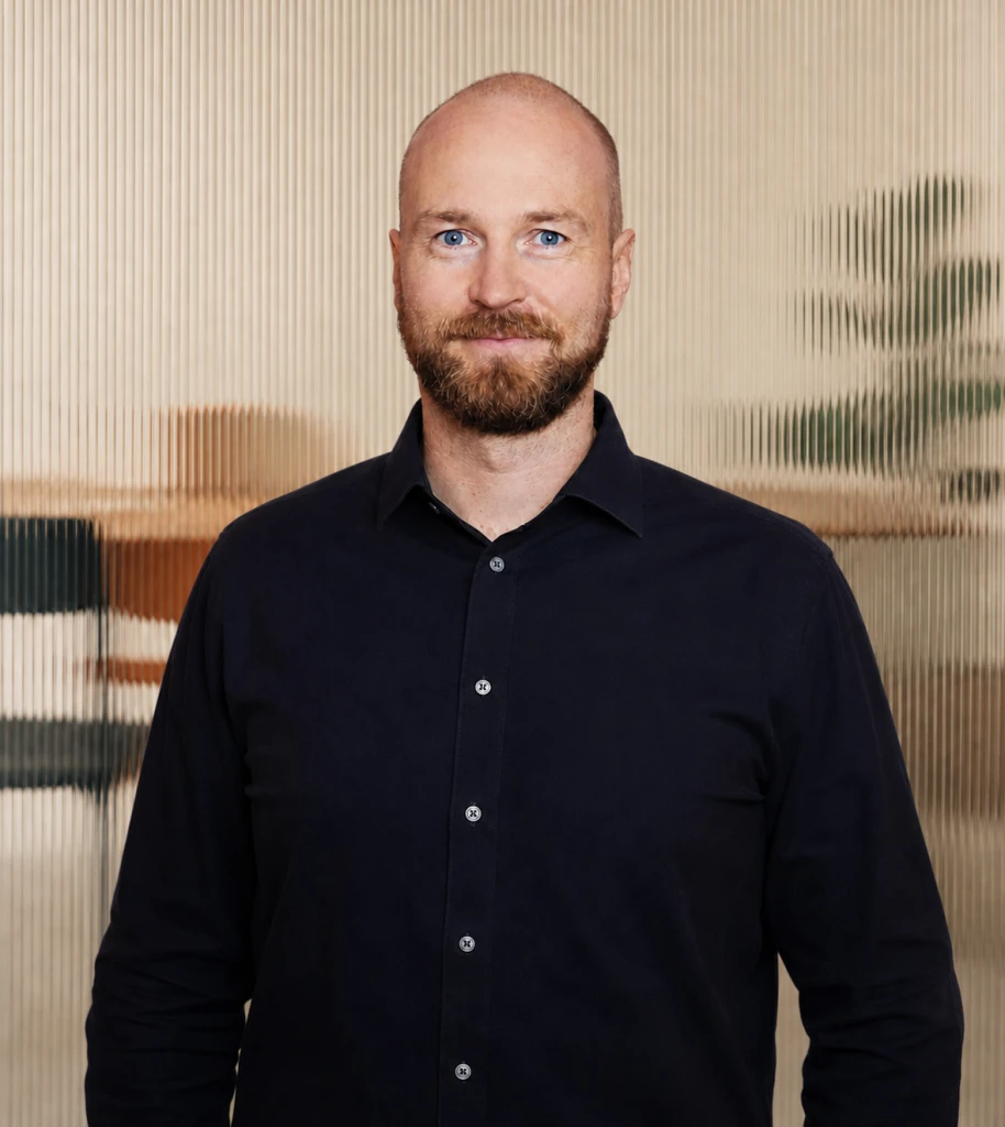 Hannes Mindt im dunklen Hemd vor einer Wand aus geriffeltem Glas.